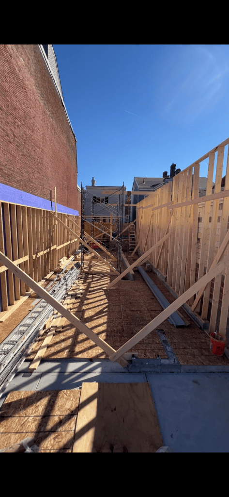 Construction site showing wooden framing and scaffolding under a clear blue sky.